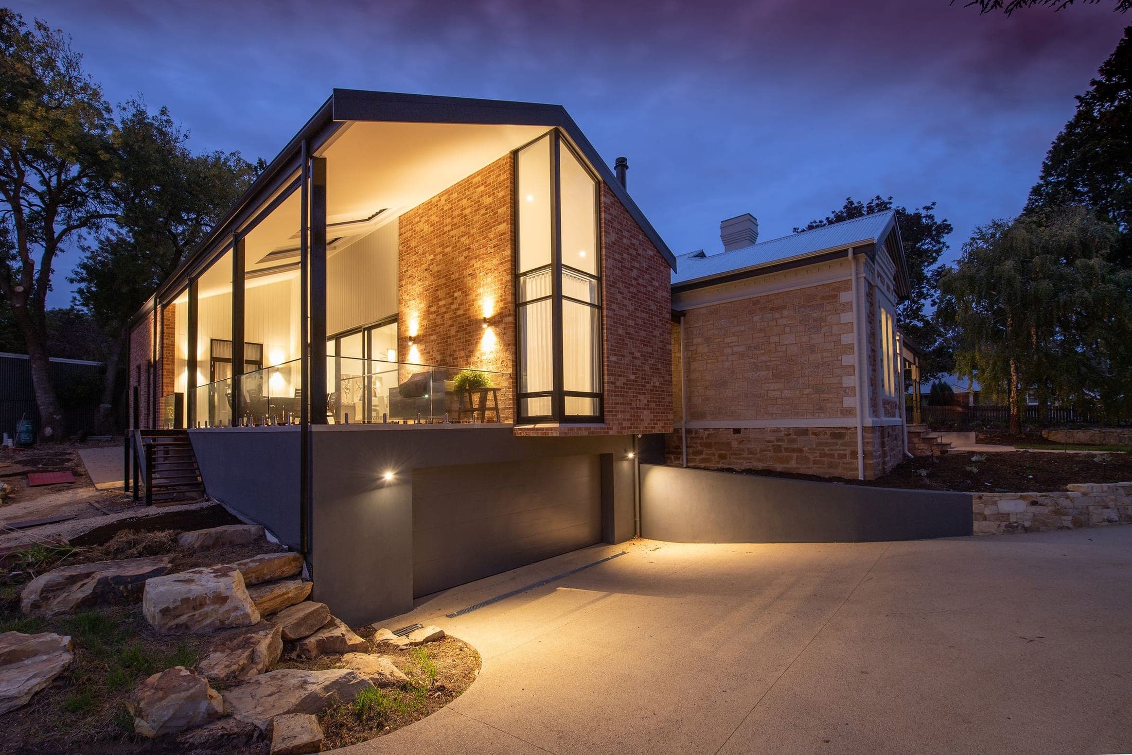 A brick and glass home extension glowing with warm light under a deep blue dusk sky